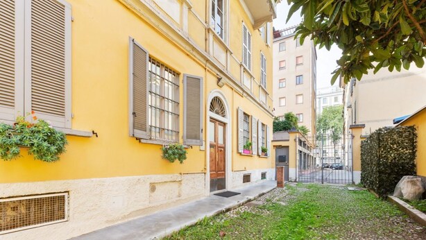 Un bâtiment jaune avec des volets, une porte et un petit jardin.