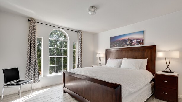 A bedroom with a large bed, a nightstand, a chair, and a window with curtains. - North East Luxury Retreat (Round Rock)