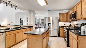 A modern kitchen with wooden cabinets, a central island, stainless steel appliances, and a black countertop. - North East Luxury Retreat (Round Rock)