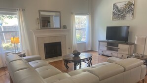 A living room with a large white sectional sofa, a fireplace, a television, and a dining table. - North East Luxury Retreat (Round Rock)