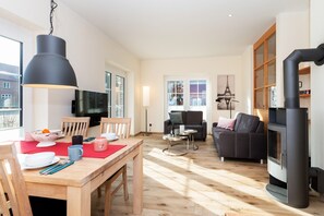A spacious living area with a dining table, chairs, a sofa, a TV, and a fireplace. - Exclusive holiday home with fireplace and sauna, terrace and beach chair, 4 persons (Vitzdorf)