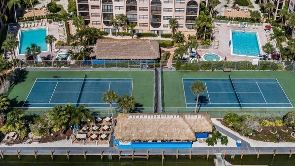 An aerial view of a hotel with two tennis courts, a pool, and a thatched-roof structure.