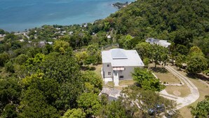 Un bâtiment d’un seul étage, doté d’un toit plat, entouré d’une végétation luxuriante et offrant une vue dégagée sur l’océan.