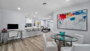 A modern living room with a glass dining table, a sofa, and a kitchen area in the background.