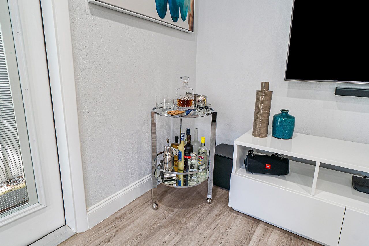 Une pièce avec un chariot en verre rempli de bouteilles, un téléviseur et un meuble blanc.