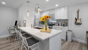 A modern kitchen with white cabinetry, a central island, bar stools, and a guitar on the wall.