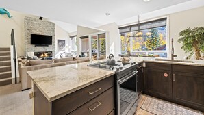 Una cocina moderna con una isla central, muebles oscuros y un amplio ventanal con vistas a árboles.