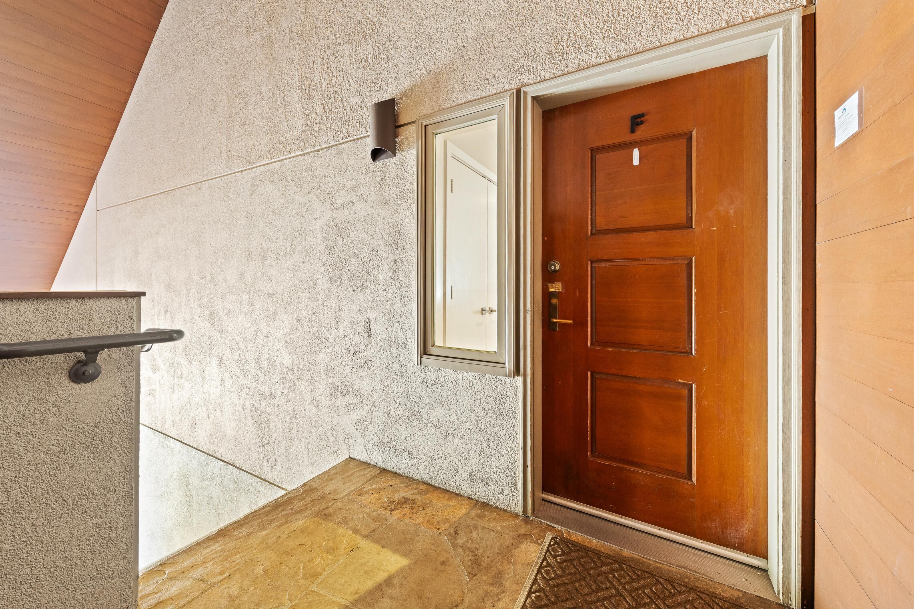 Une porte en bois avec une plaque portant un numéro, un mur à la texture particulière et une petite fenêtre.
