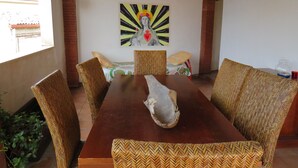 A dining area with a wooden table and woven chairs, a painting on the wall, and a window with a view of buildings. - Beautiful terrace and peace of mind in the city centre (Palermo)