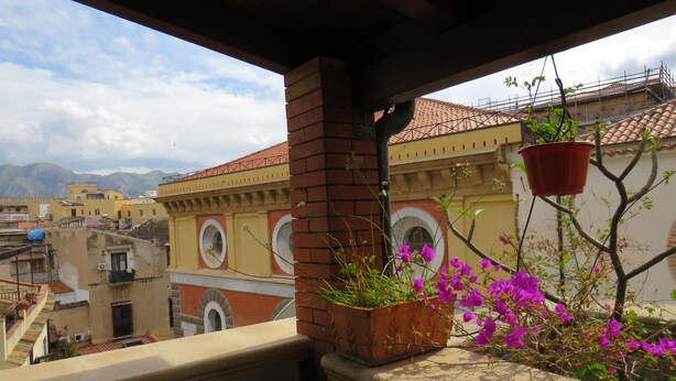 A balcony with a view of a cityscape, a hanging planter with flowers, and a brick pillar. - Beautiful terrace and peace of mind in the city centre (Palermo)