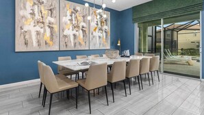 A dining area with a marble table and beige chairs, a large abstract painting on the wall, and a view of a pool through glass doors. - Cosmic Home w Space Theme BR, Theater, Arcade, Game Loft, Pool - Mins to Disney (Davenport)