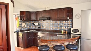 Una cucina con mobili in legno scuro, zoccolo in piastrelle, isola integrata con sgabelli e frigorifero.