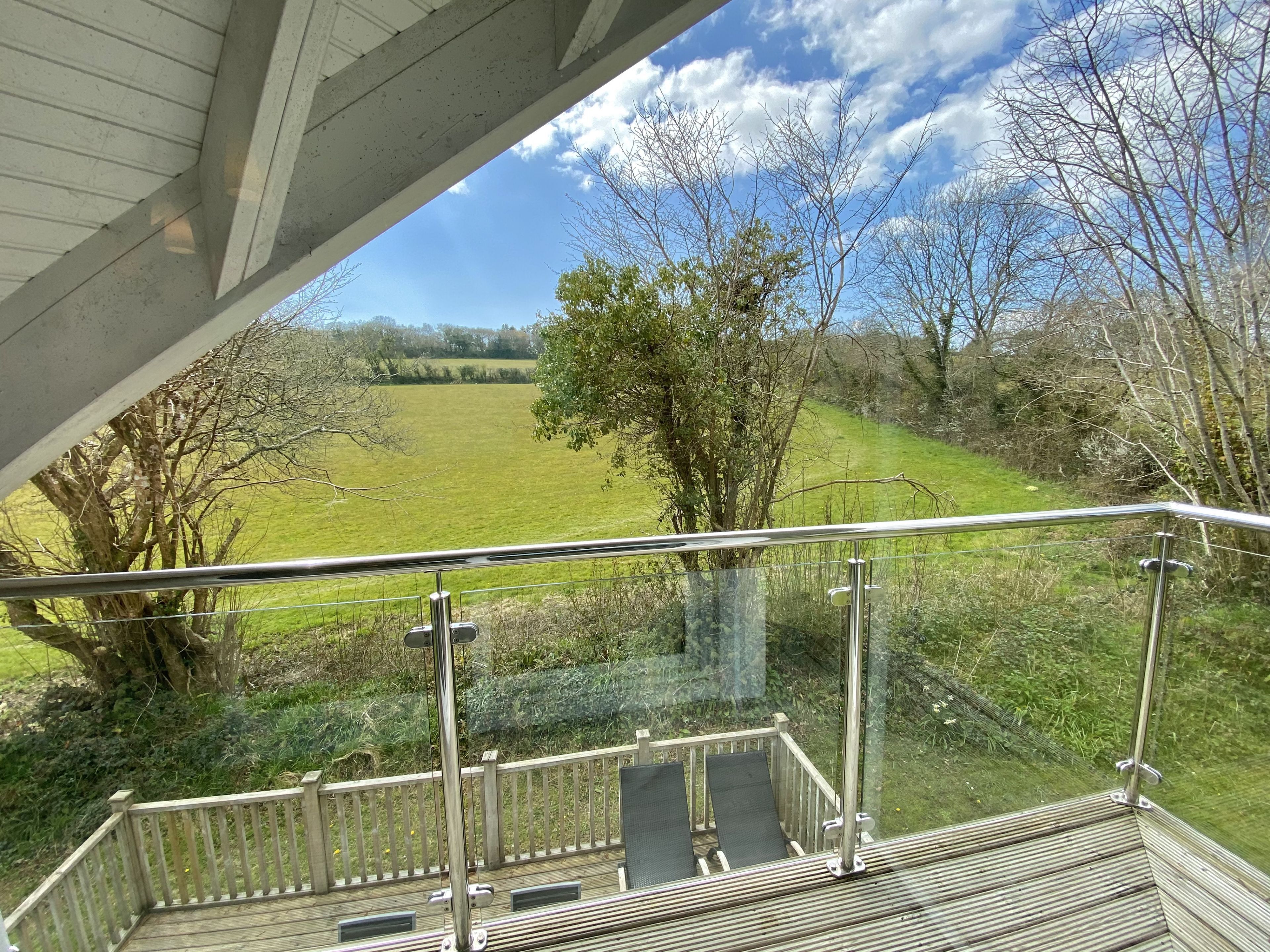 A balcony with a view of a green field and trees.