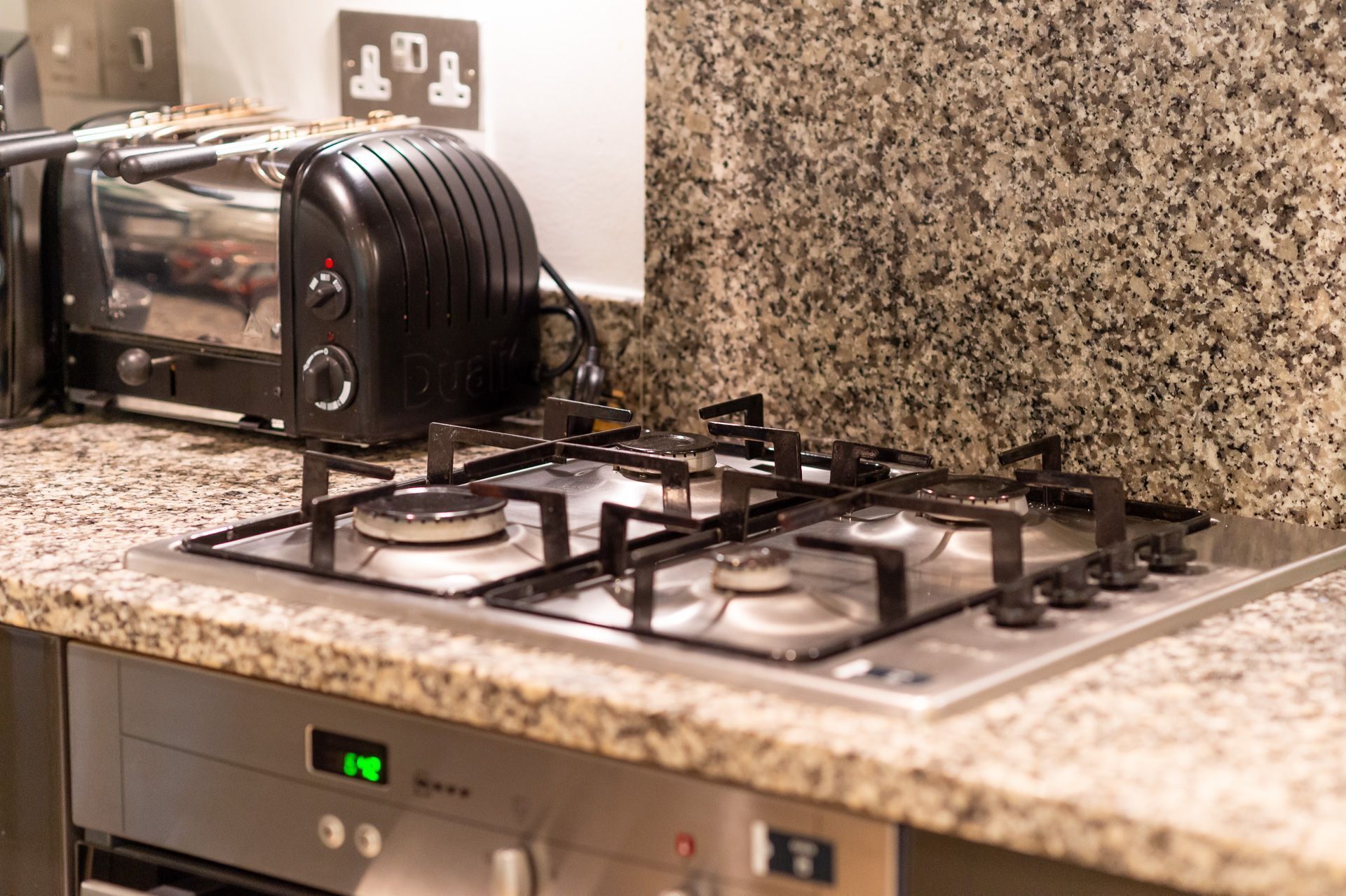 A kitchen with a gas stove, a toaster, and a digital clock displaying 12:48.
