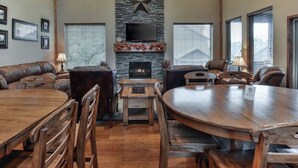 Amplia sala de estar con chimenea de piedra, sofás de cuero y una mesa de comedor de madera.