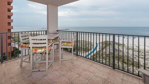 A balcony with two white chairs and a table, overlooking a beach with a sandy path and a blue slide.