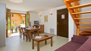 A modern living room with a wooden staircase, a dining area with wooden furniture, and a TV on a wooden cabinet.