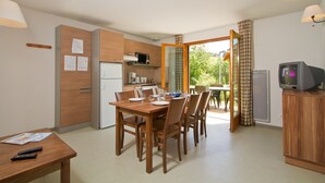 A compact kitchen with a dining area, wooden cabinets, a microwave, and a television.