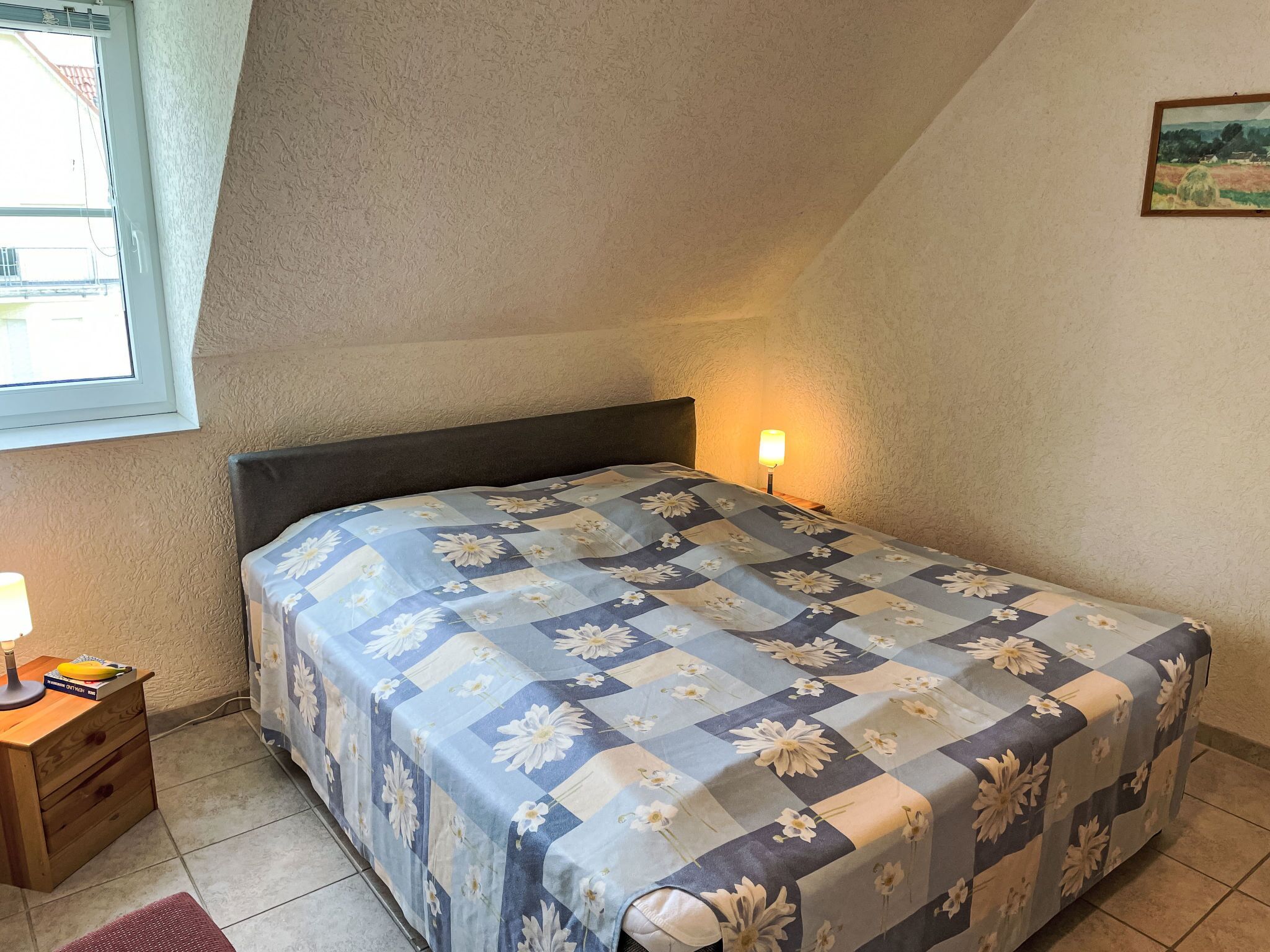 Une chambre à coucher avec un lit, une table de chevet, une lampe et une fenêtre.