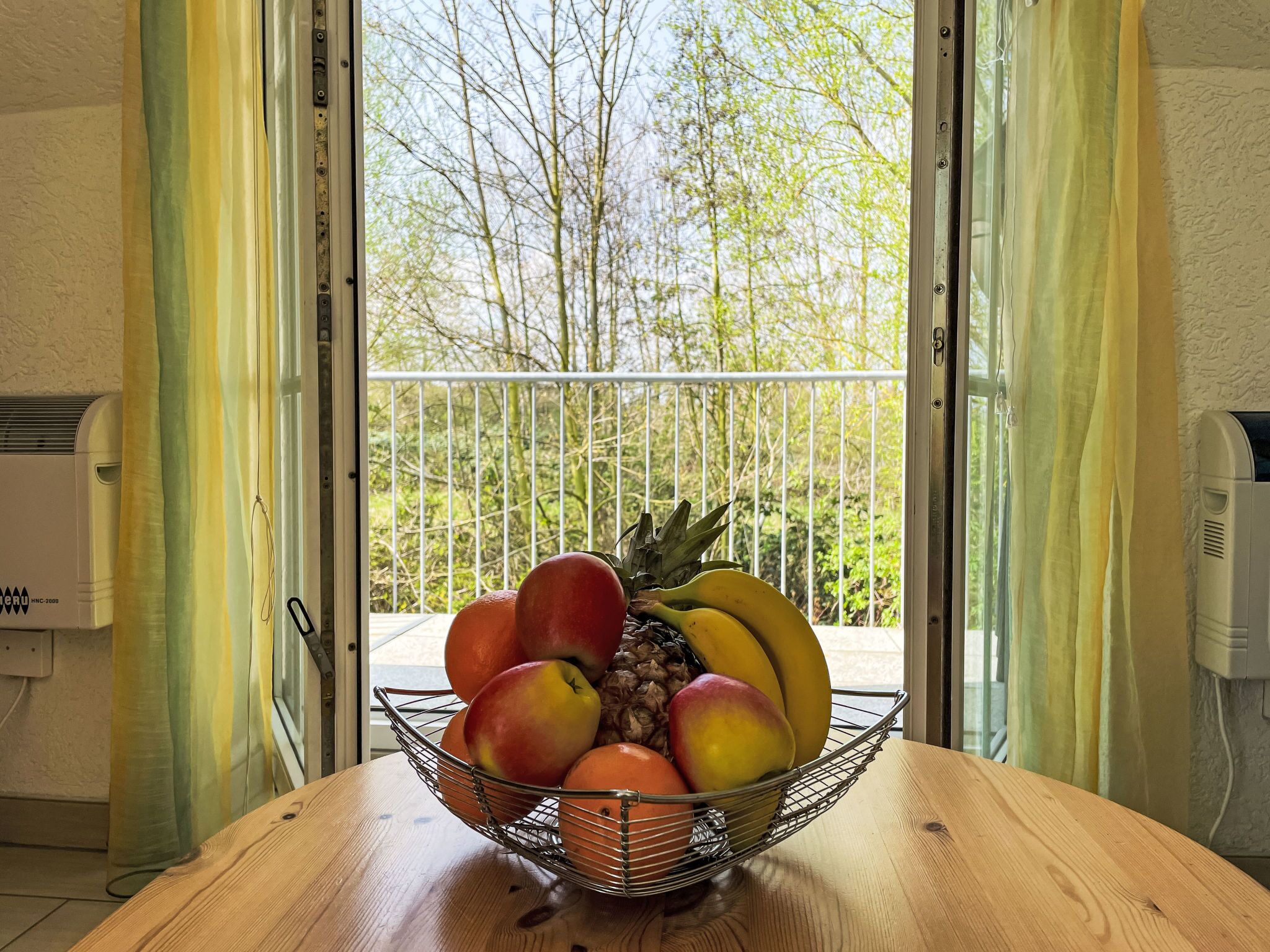Een houten tafel met een fruitmand met appels, sinaasappels en bananen.