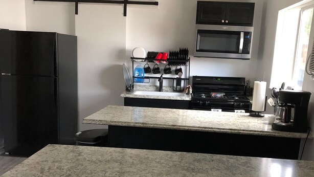 Una cocina con encimera de granito, un refrigerador negro, una estufa y un microondas.