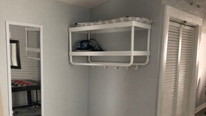 Habitación de esquina con una mesa blanca, un estante blanco y un armario con contraventanas blancas.