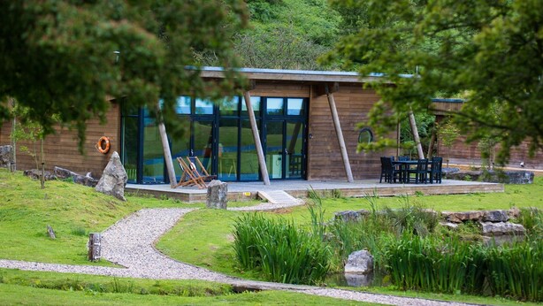 Een modern gebouw met een glazen gevel, houten buitenkant en een terras met zitplaatsen.