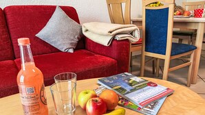 A living room with a red sofa, a wooden table with a magazine, fruits, and a bottle of pink drink. - Gollwitzer Park (Insel Poel) by Interhome (Gollwitz (Insel Poel))