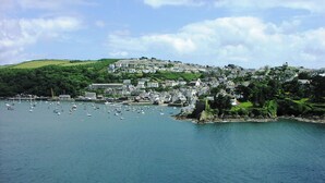 A coastal town with a harbor filled with boats, surrounded by green hills and residential buildings. - St Catherines Court No 7 (Fowey)