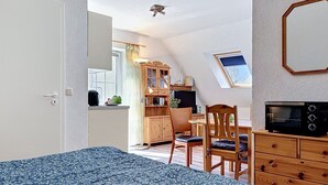 Une chambre avec un lit, un bureau avec un ordinateur, une télévision et un coin cuisine.