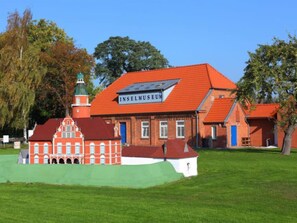 Experience the Inselmuseum's traditional architecture, featuring a distinctive red-tiled roof and a green-tiled tower, set amidst a serene green lawn and lush trees.