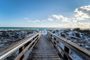 Une promenade en bois qui mène à une plage bordée de dunes de sable, avec l’océan en toile de fond.