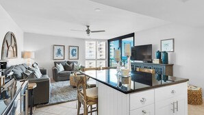 Eine moderne Küche mit Kochinsel, ein Essbereich mit Holztisch und ein Wohnzimmer mit Sofa und Fernseher.