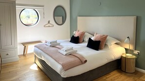 A neatly made bed with pillows and a blanket, a bedside lamp, a round mirror, and a wooden hanger on the wall. - A yorkshire dale that sleeps 6 guests  in 3 bedrooms (Richmond)