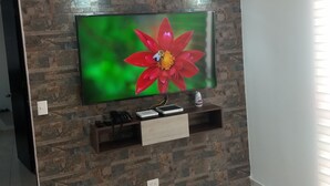 A flat-screen TV mounted on a stone-patterned wall with a wooden shelf below.