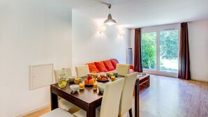 A dining area with a wooden table, white chairs, and a red sofa. There are bowls of fruit and a bottle of juice on the table. - Appart Cosy avec Terrasse! Accès Sauna | Pistes (La Féclaz)