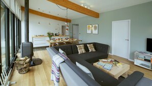 Een moderne woonkamer met een bank, salontafel en televisie. Er is een keukenhoek met een eettafel en stoelen.