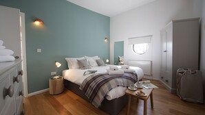 Een slaapkamer met een bed, nachtlampjes, een nachtkastje met een kopje en een bord, en een koffer.