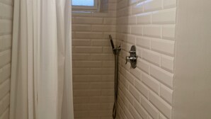 Um pequeno banheiro com azulejos brancos, chuveiro, janela e cortina.
