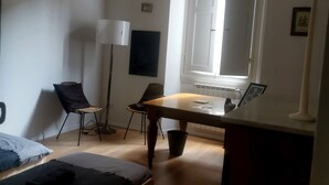 Quarto com cama, escrivaninha, duas cadeiras, abajur, janela e radiador.