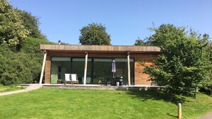 A modern building with large glass windows, a wooden deck, and outdoor seating.