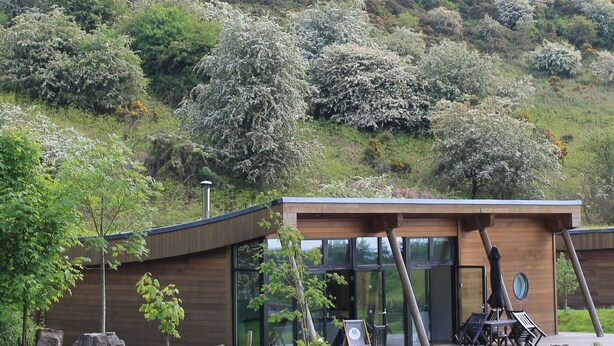 A modern building with a flat roof, large windows, and a patio area with outdoor seating.