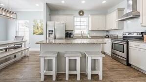 Eine moderne Küche mit weißen Schränken, einer Granitarbeitsplatte, einem Edelstahlkühlschrank, einem eingebauten Backofen und einer Kaffeemaschine.