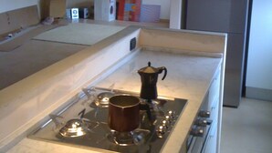 Eine Küche mit Gaskochfeld, Kaffeemaschine, Kühlschrank und einem farbenfrohen abstrakten Gemälde an der Wand.