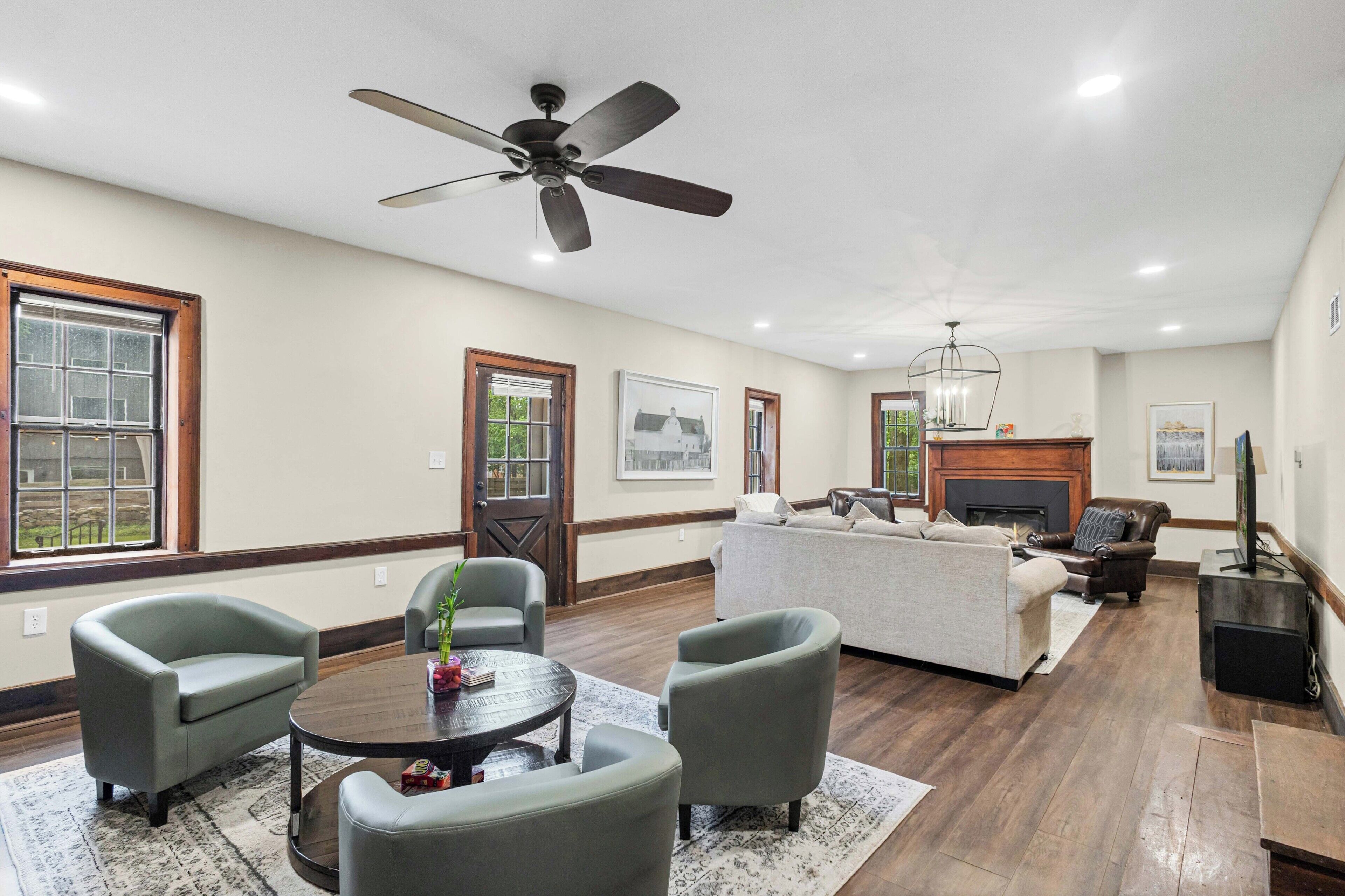 A spacious living room with a fireplace, a ceiling fan, and a large window.
