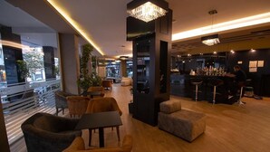 Un moderno vestíbulo de hotel con asientos mullidos, una zona de bar y amplias ventanas con vistas a la ciudad.