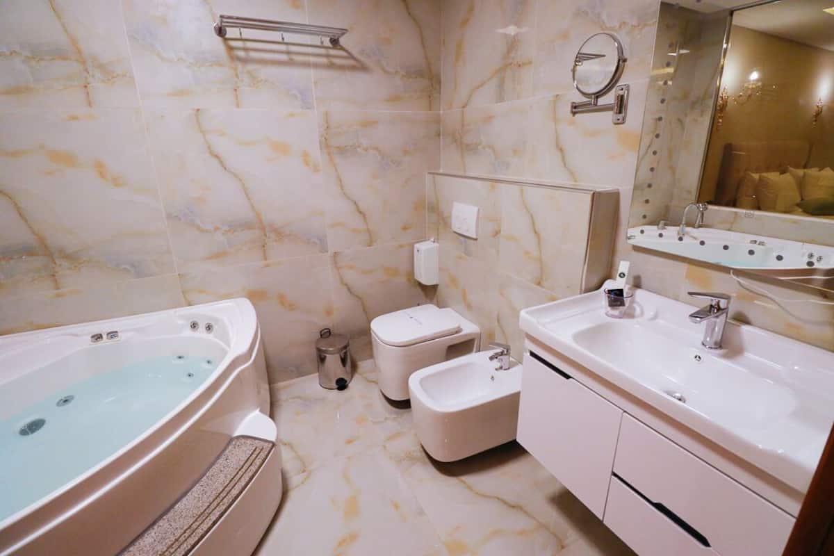 A bathroom with a marble floor, a bathtub, a toilet, a bidet, and a sink with a mirror above it.