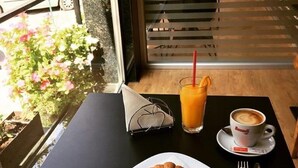 Una mesa con un croissant, un vaso de jugo de naranja y una taza de café, con vista a la calle.