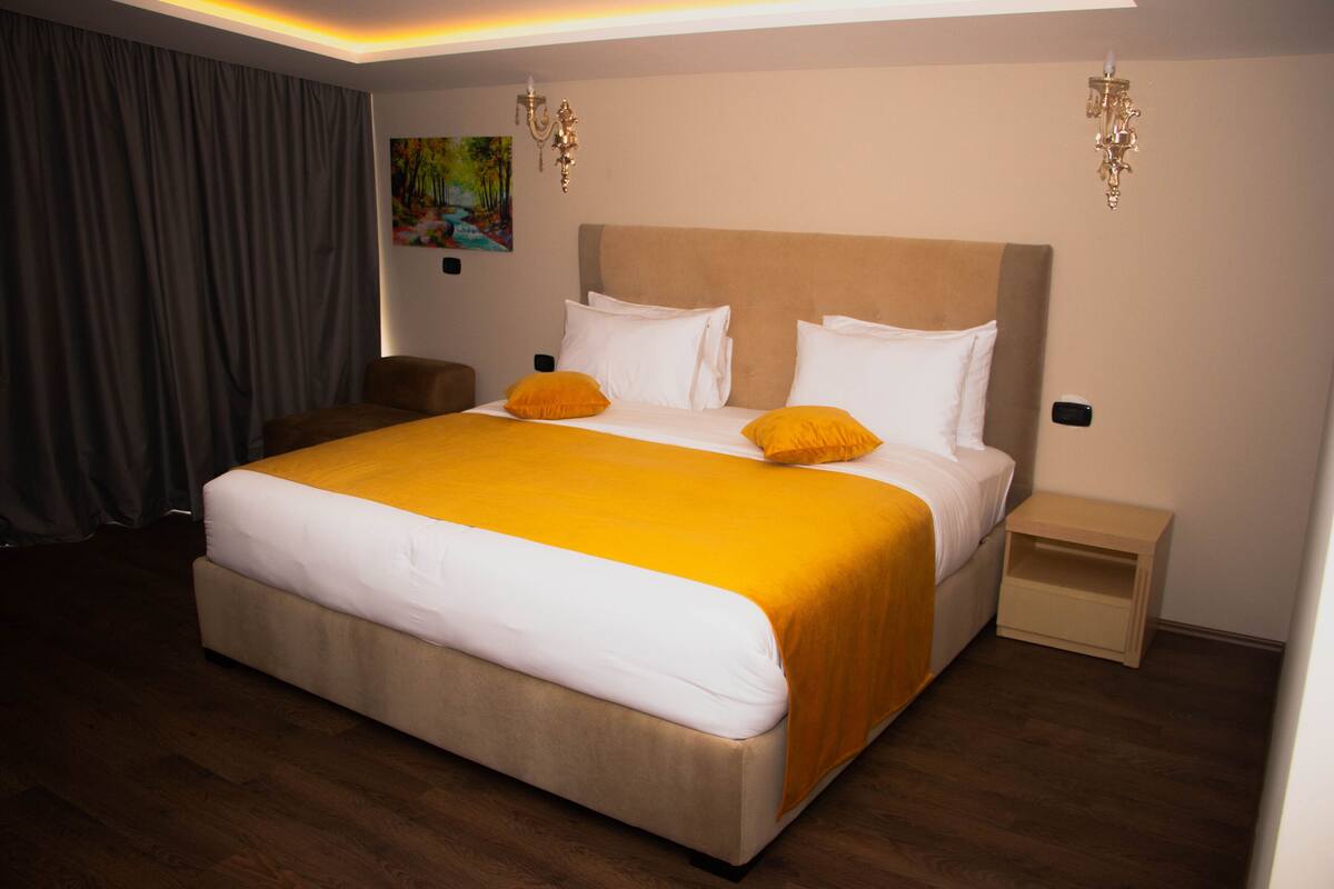 A hotel room with a large bed, a bedside table, a chair, and a painting on the wall.