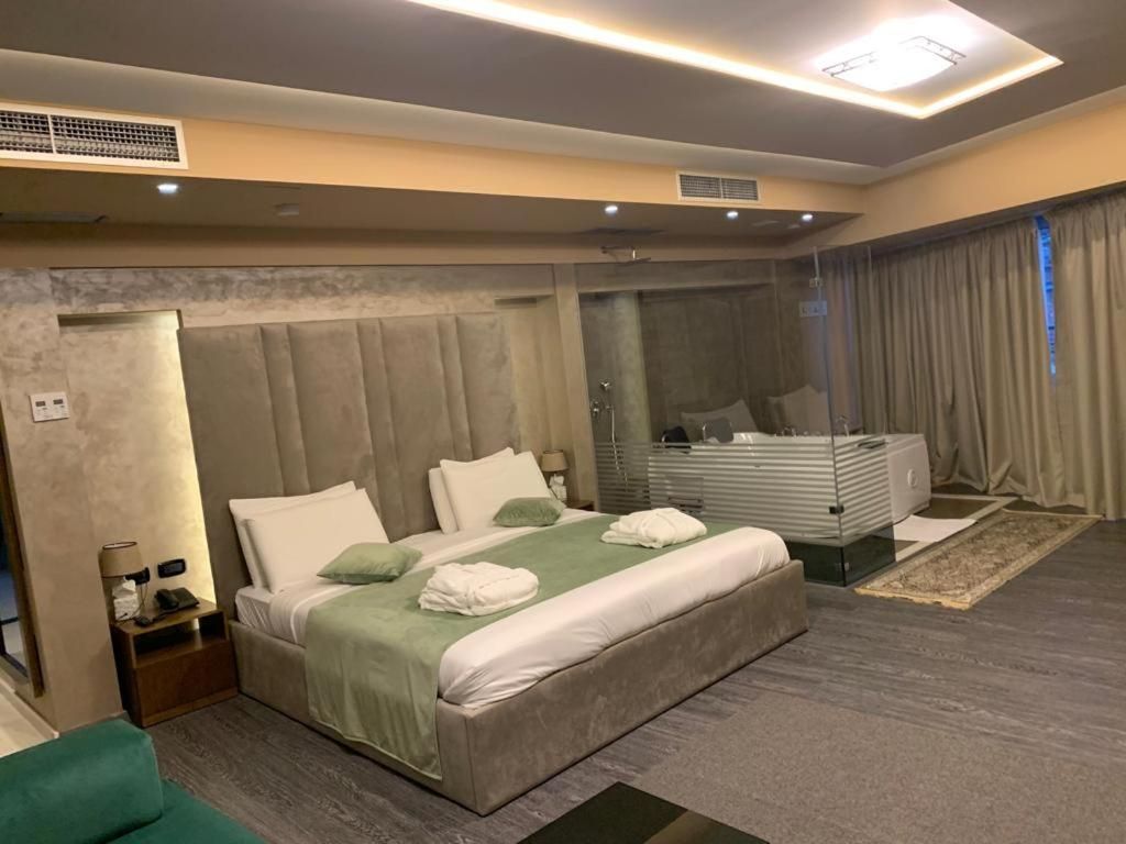 A modern hotel room with a large bed, a vanity with a mirror, and a separate shower area.